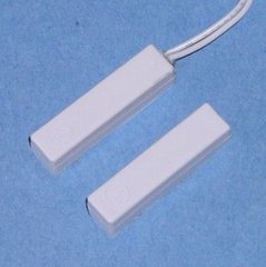 Two white 1 1/4 inch surface mount magnetic alarm contact switches with one featuring an attached white cable